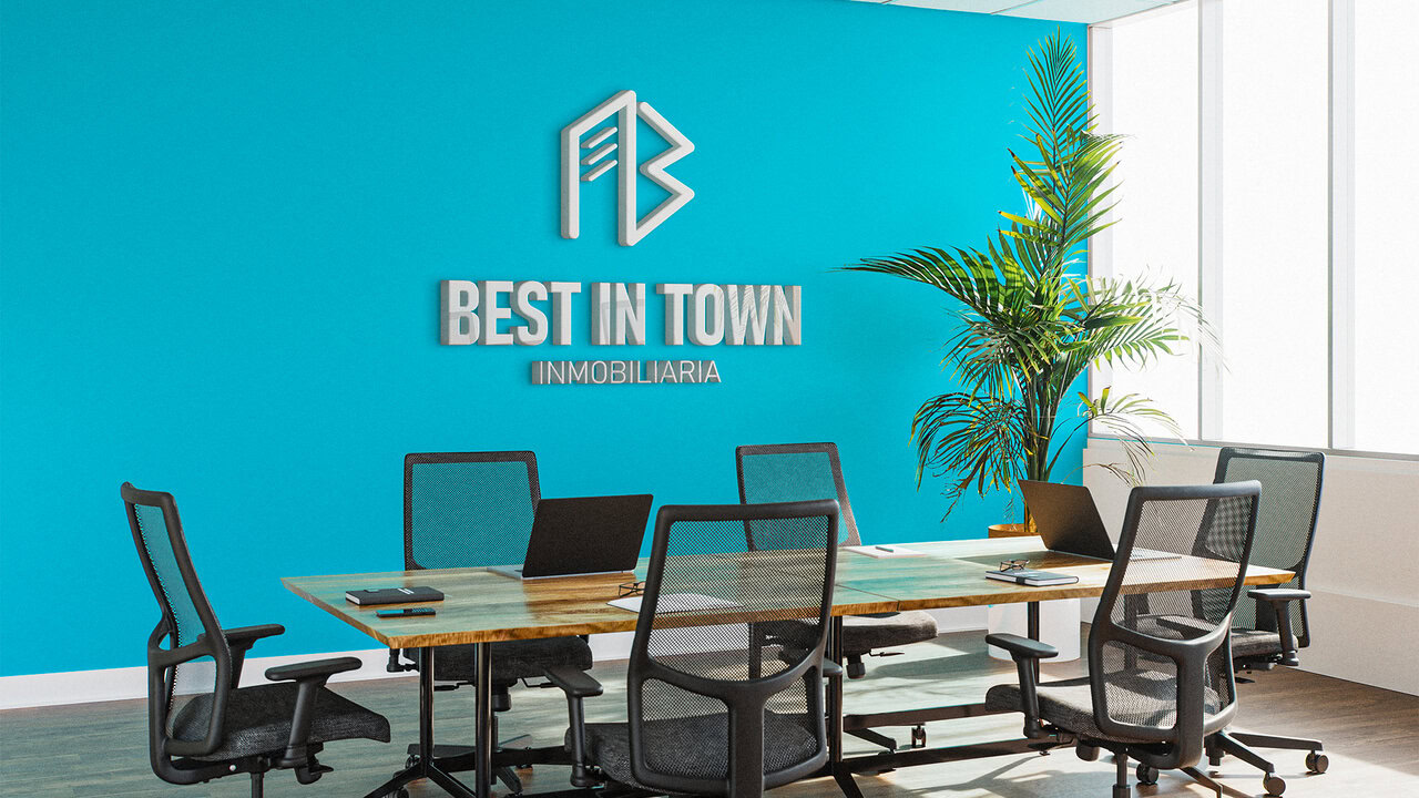Nebly_BestInTown_Oficina_1 Oficina moderna con pared azul de fondo, en el medio del espacio hay una mesa de madera con sillas de oficina alrededor, ambiente empresarial y juvenil.