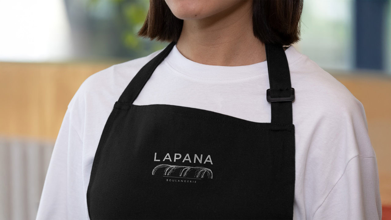 Nebly_LAPANA_Mandil_1920x1080 Mandil negro con el logotipo de LAPANA bordado en blanco. Diseño de uniforme para panadería artesanal.